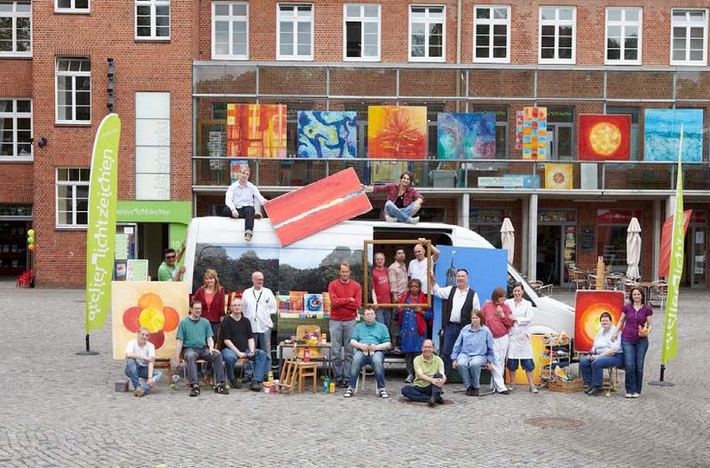 Gruppenfoto des Ateliers Lichtzeichen vor einem Klinkergebäude mit vielen bunten Bildern