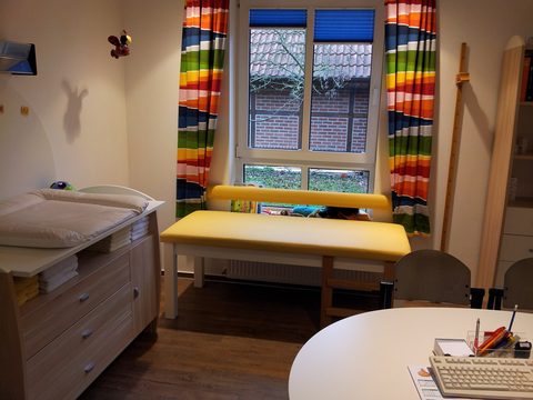 Kinderzimmer mit Wickelkommode, gelber Untersuchungsliege und bunten Vorhängen