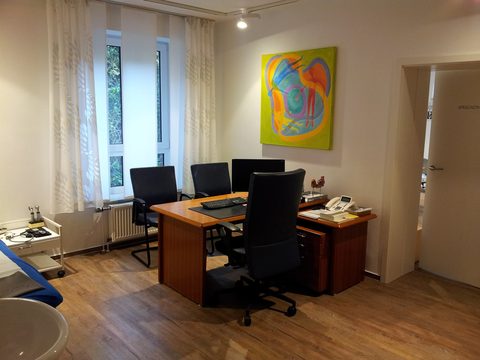 Helles Sprechzimmer mit Schreibtisch, Stühlen und einem bunten Gemälde