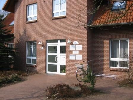 Eingang der Praxis am Weidenweg 16, ein Klinkerbau mit weißer Glastür